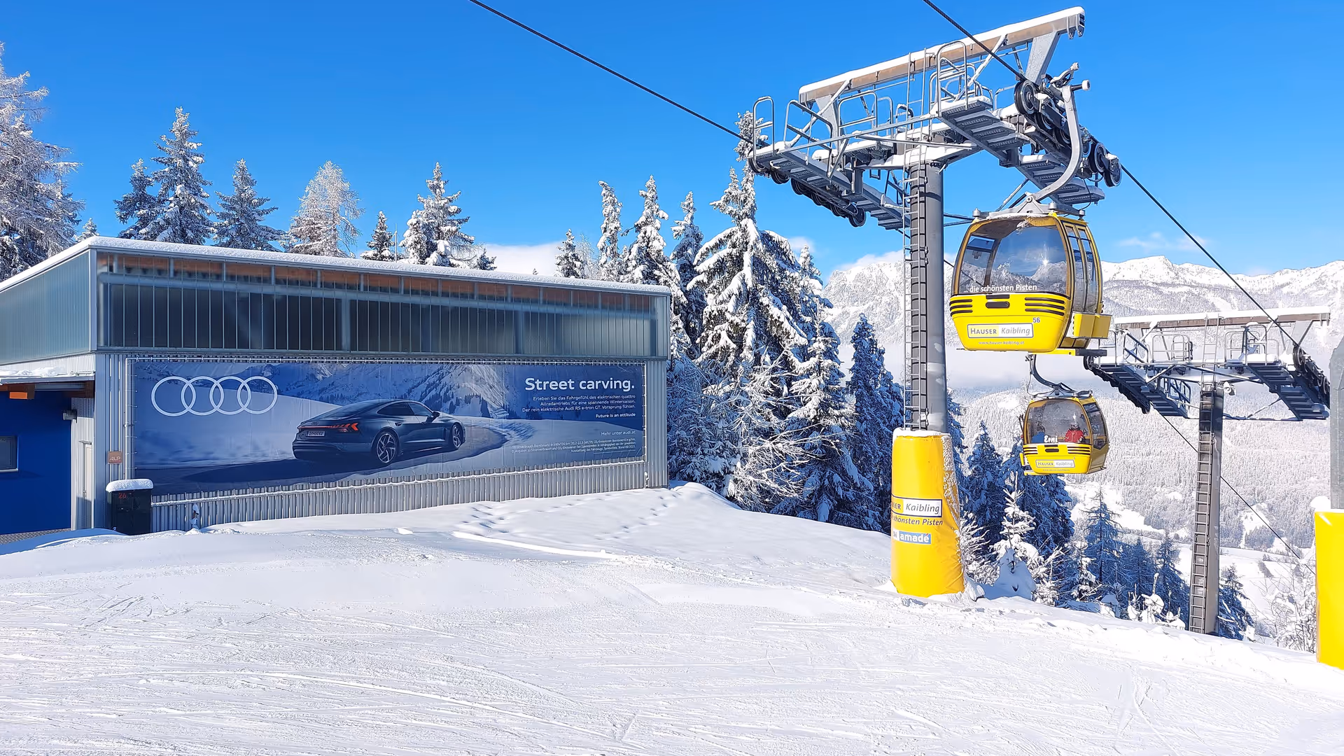 OOH-Werbefläche im Skigebiet Hauser Kaibling in den Alpen: großformatige Audi-Werbung an der Liftstation vor verschneiter Bergkulisse